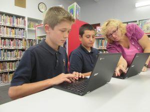 Judy DeLorenzo, library and media specialist at Holy Cross School, works with sixth-graders Luke Boule and Daniel Stark on Sept. 21. - SUN PHOTO | TOM MAGUIRE